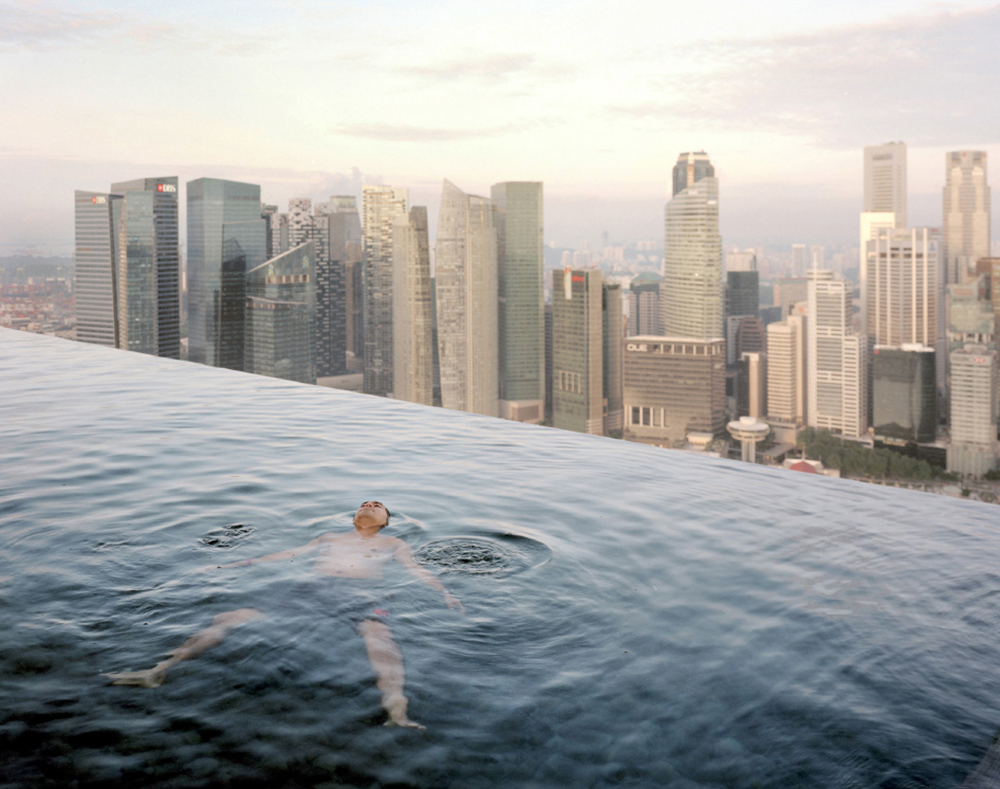 A man floats in the 57th-floor swimming pool of the Marina Bay Sands Hotel, with the skyline of the Singapore financial district behind him. 2013 Paolo Woods & Gabriele GalimbertiÑINSTITUTE