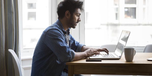 banking-blog-young-man-sitting-at-a-table-near-windows-looking-at-a-laptop