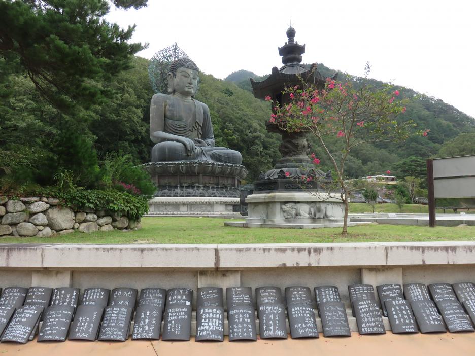 Socha Budhu pri vstupe do Národného parku Seoraksan. Mená donátorov sú uvedené na škridliach, poukladaných pod múrikom.