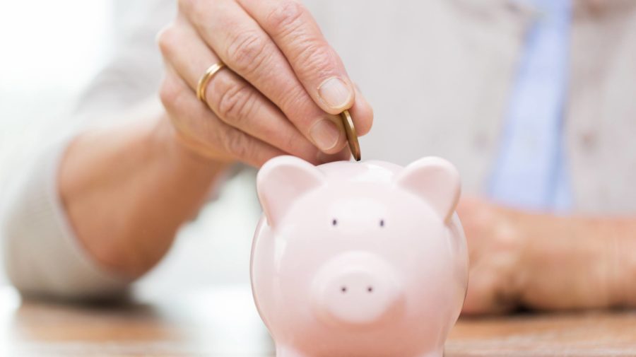 senior-woman-hand-putting-money-to-piggy-bank