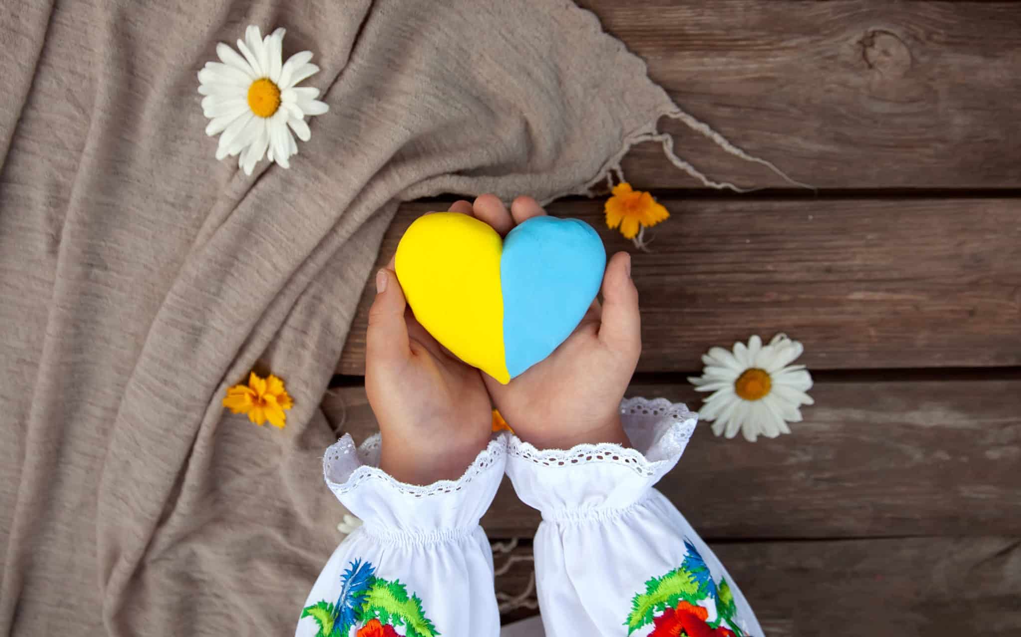 iStock-12972A yellow and blue heart in the hands of a child in an embroidered shirt, against the background of a rough wooden table and daisies.Unity Day, Independence Day of Ukraine, Embroidery Day43431