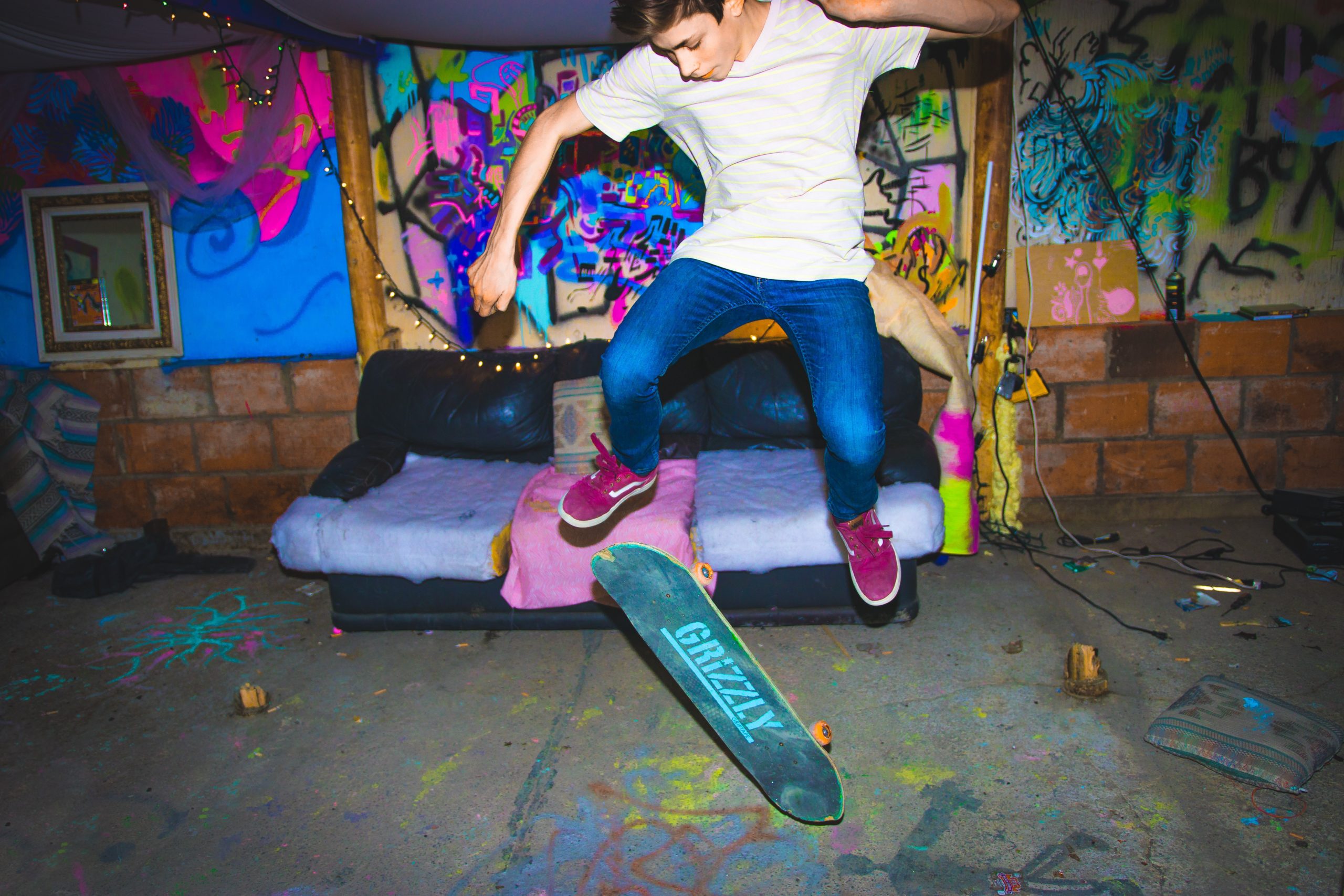Chlapec na skateboarde skáče pred gaučom a posprejovanou stenou