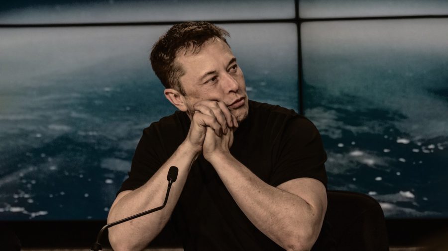 Elon Musk sedí pred mikrofónom so zloženými rukami