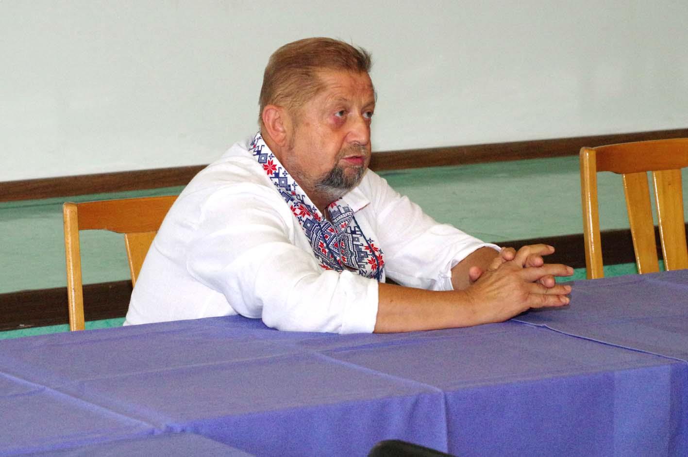 Štefan Harabin v ľudovom kroji sedí s rukami na stole s fialovým obrusom