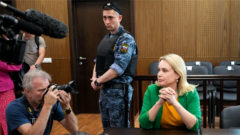 Marina Ovsiannikovová sedí v súdnej sieni obklopená novinármi pred pojednávaním v Moskve. Hrozí jej až 10. rokov väzenia
