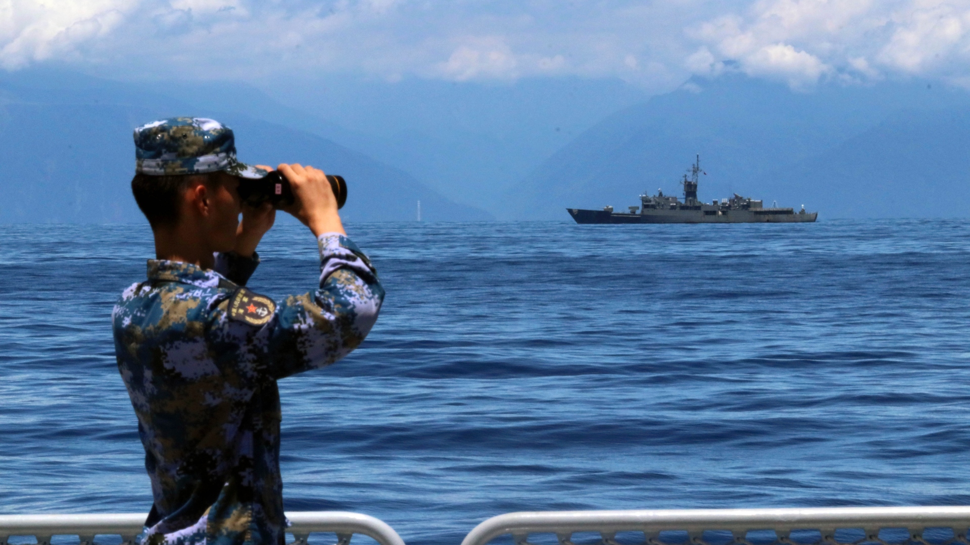 Na archívnej snímke z 5. augusta 2022, čínsky vojak sa pozerá cez ďalekohľad počas vojenských cvičení, vzadu sa plaví taiwanská fregata. Čínska armáda v stredu oznámila, že "úspešne dokončila rôzne úlohy" v okolí Taiwanu, kde pred týždňom spustila rozsiahle vojenské cvičenia.