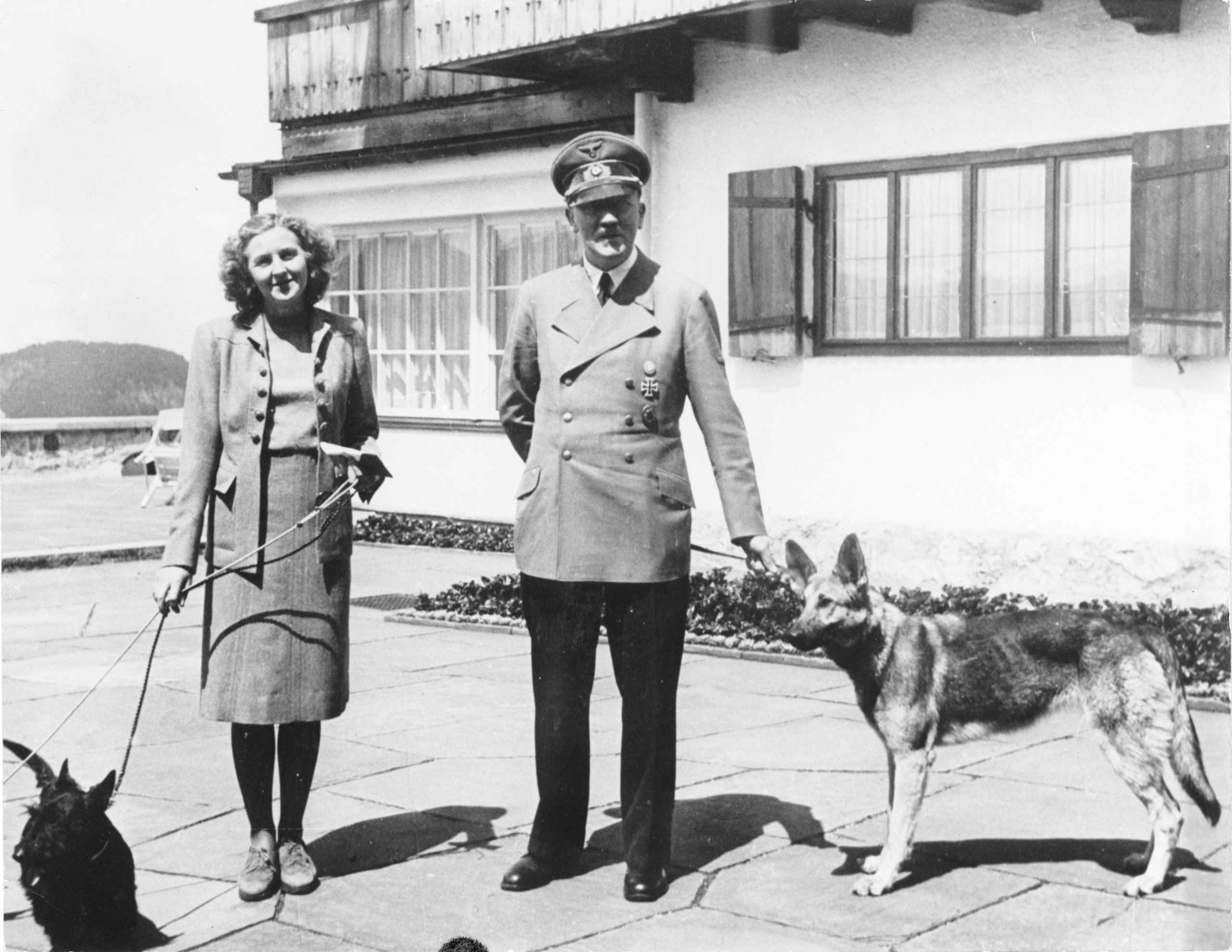 Adolf Hitler a Eva Braun stoja pred domom, každý z nich má na vôdzke psa