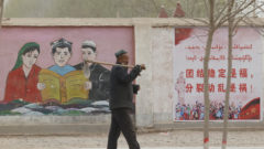 farmár prechádza pred propagadistickým billbordom v Číne, ktorý zobrazuje príslušníkov etnických menšín ako čítajú ústavu.