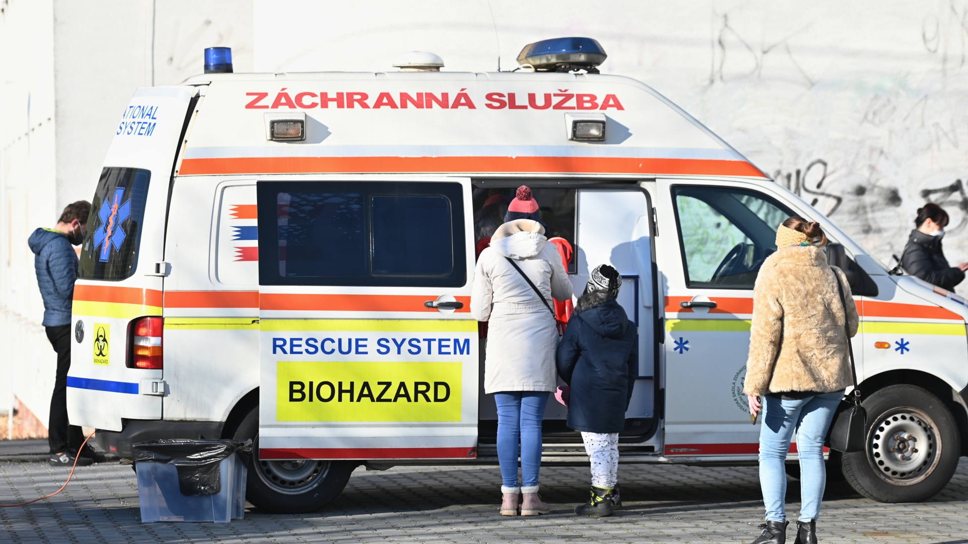 Na snímke je sanitka a ľudia, ktorí sa nechávajú testovať na Covid.