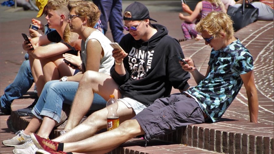 tínedžeri sedia vonku s mobilmi v ruke