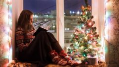 mladá žena na vianoce sedí pri okne a vianočnom stromčeku a číta knihu