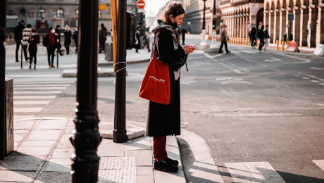 Žena s mobilom v ruke stojí pred priechodom pre chodcov