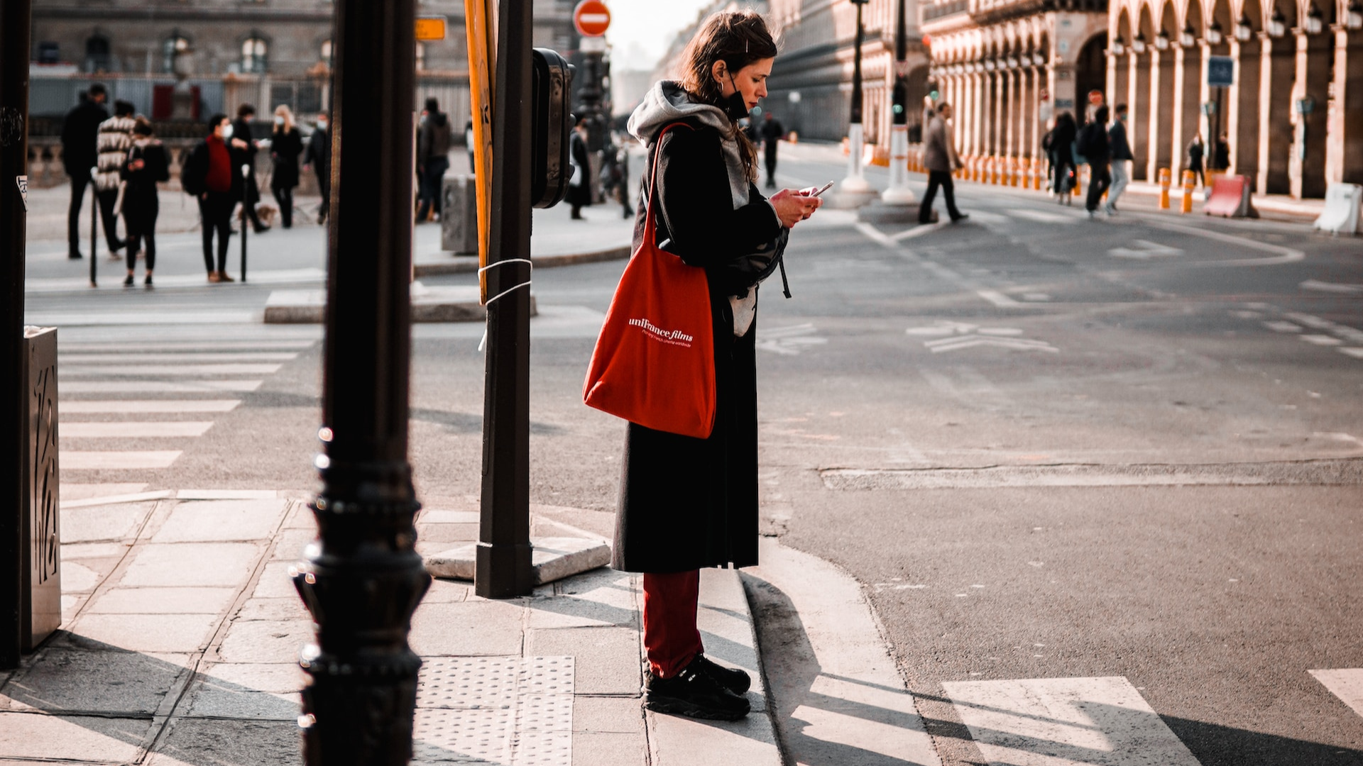 Žena s mobilom v ruke stojí pred priechodom pre chodcov