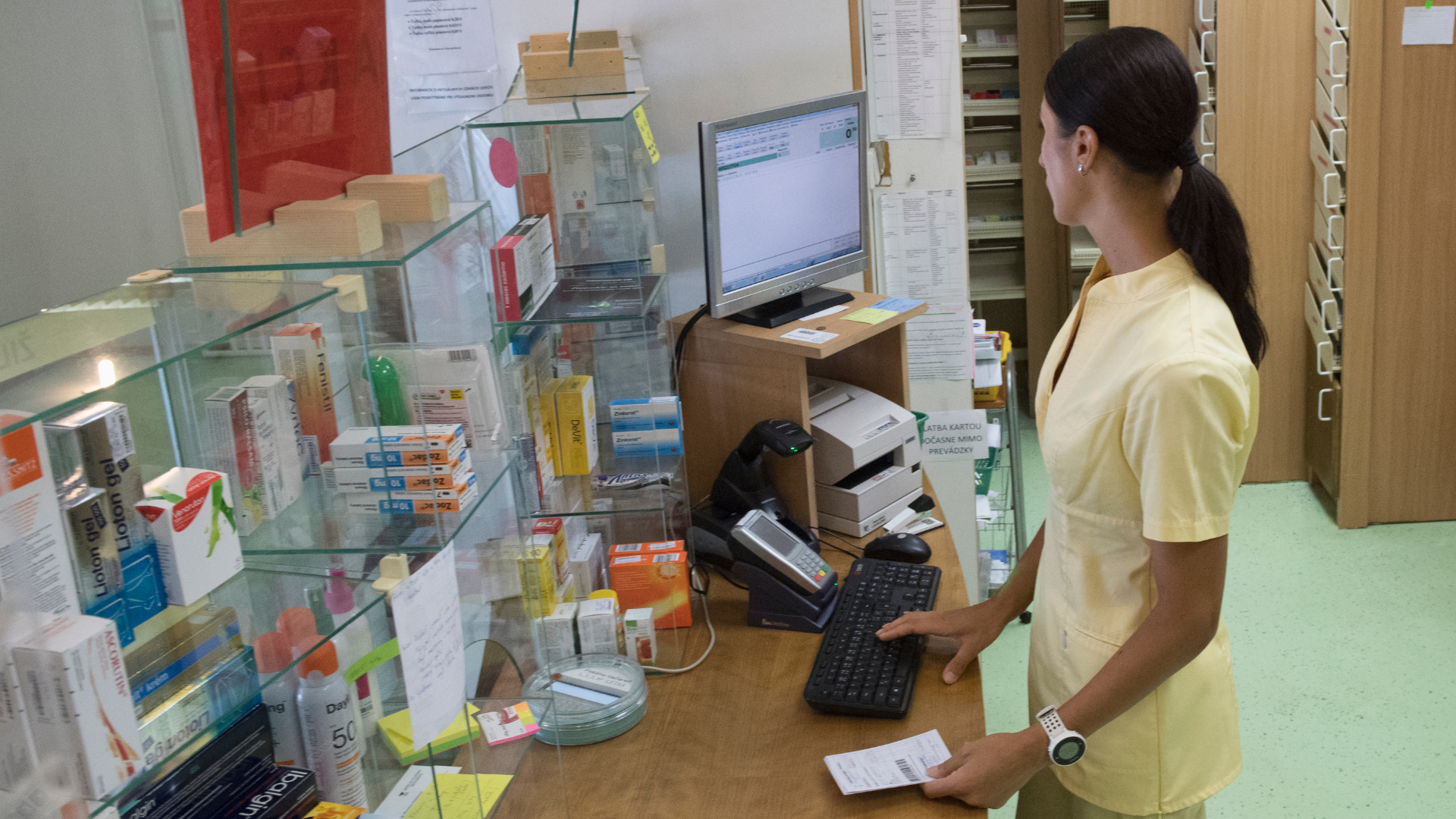 Pracovníčka v lekárni za pokladňou hľadá v systéme recept.