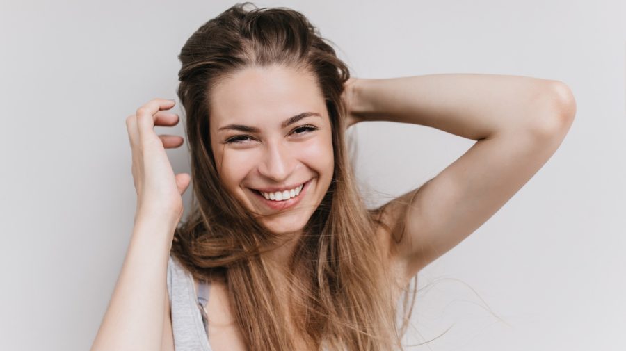 Žena s úsmevom na tvári si prehrabuje rukou vlasy