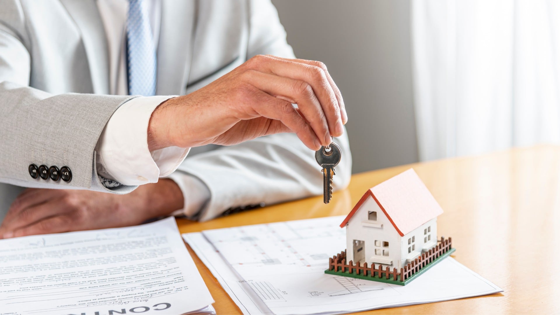 Ruka, ktorá drží kľúč nad miniatúrou domčeku.