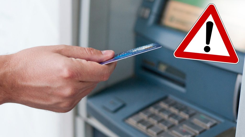 Ruka, ktorá drží bankomatovú kartu pri bankomate.