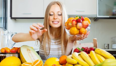Žena drží misku s ovocím a vyberá do nej ďalšie.