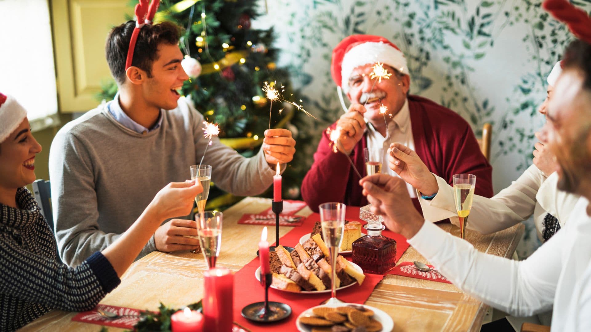 Ľudia za vianočným stolom držia prskavky a smejú sa.