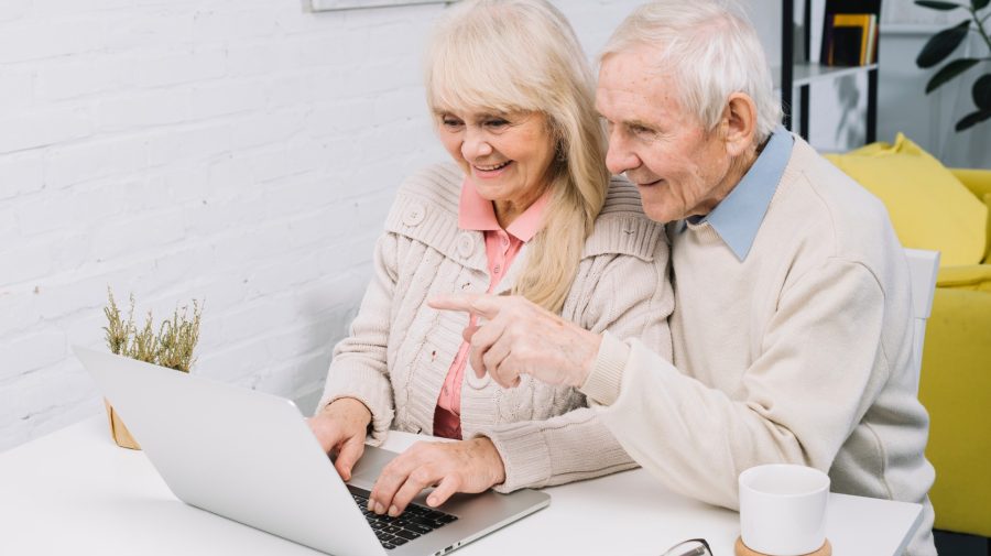 Starší muž so ženou sa pozerajú do notebooku a usmievajú sa.