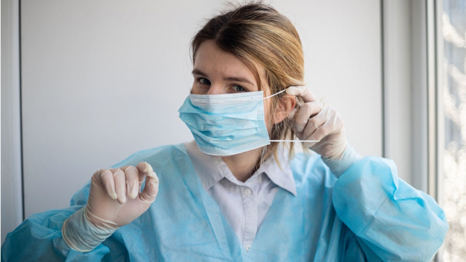 Žena v nemocničnom plášti si nasadzuje rúško.