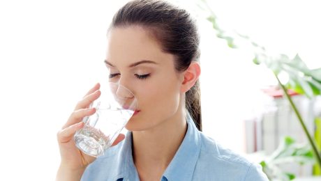 Žena pije vodu z pohára.