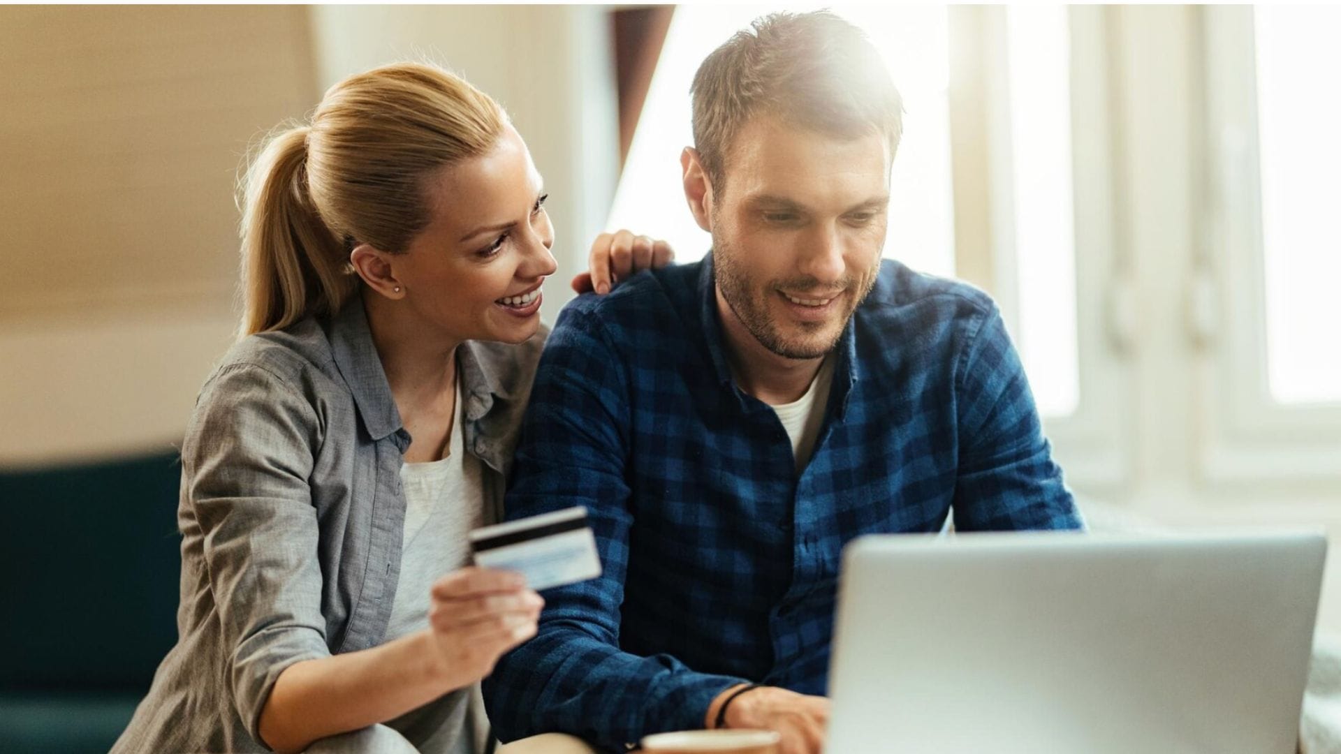Žena ukazuje kreditku mužovi, ktorý robí niečo na notebooku.