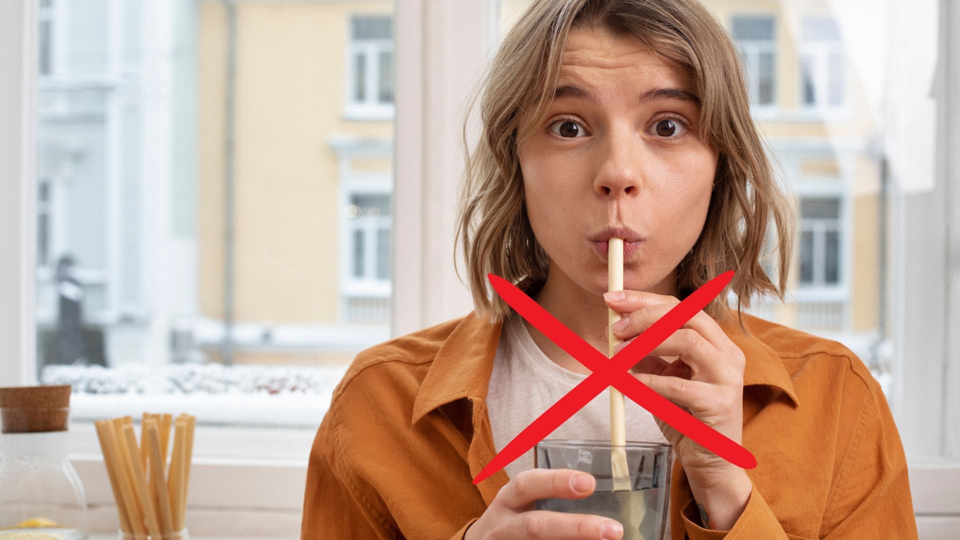 Žena pije papierovou slamkou vodu z pohára.