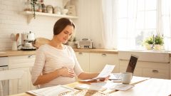 Tehotná žena sedí za stolom a drží papier v ruke.