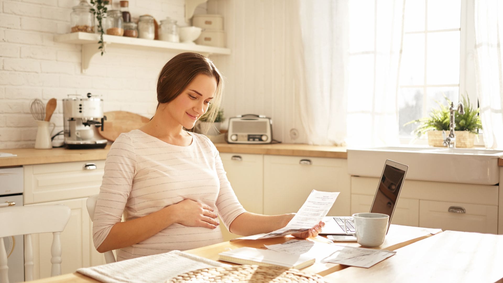 Tehotná žena sedí za stolom a drží papier v ruke.