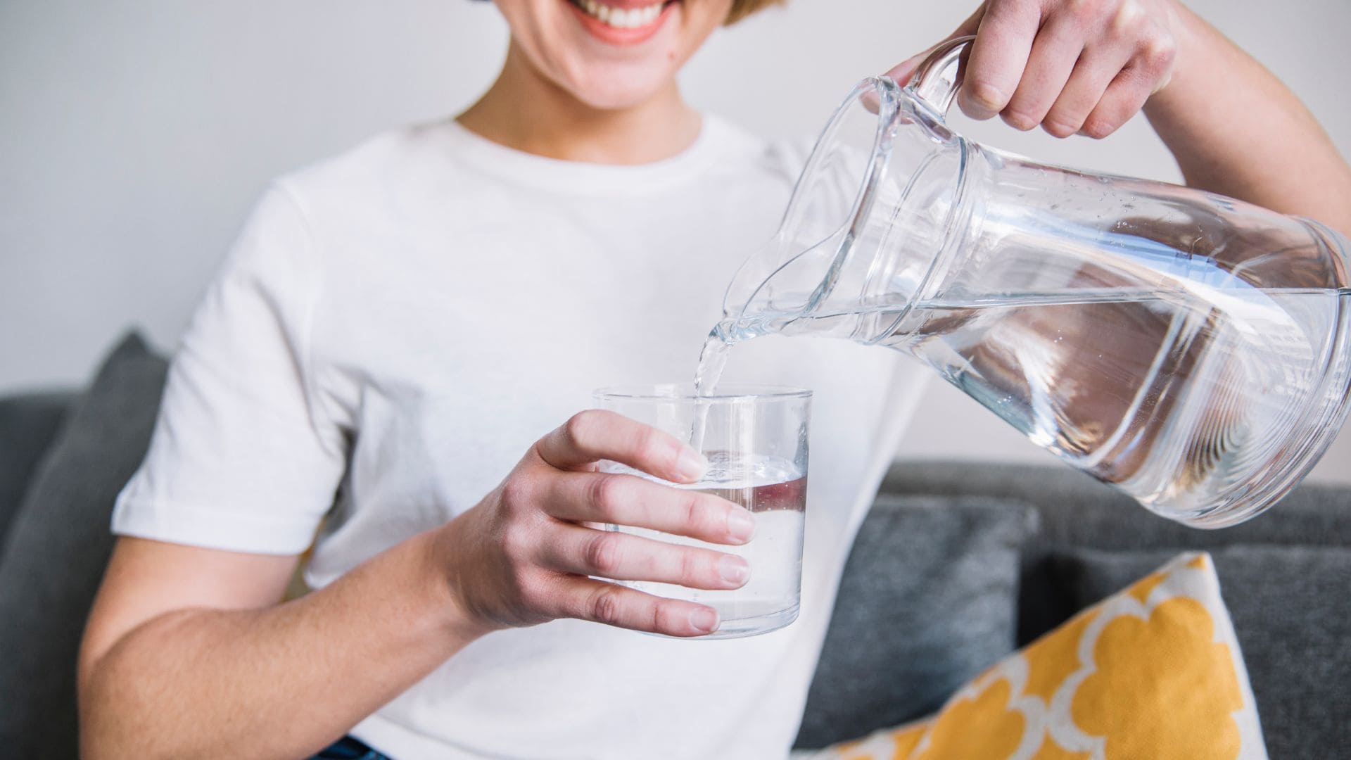 Žena si nalieva vodu z džbánu do pohára.