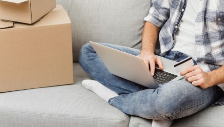 Muž na gauči má notebook na kolenách a drží kartu.