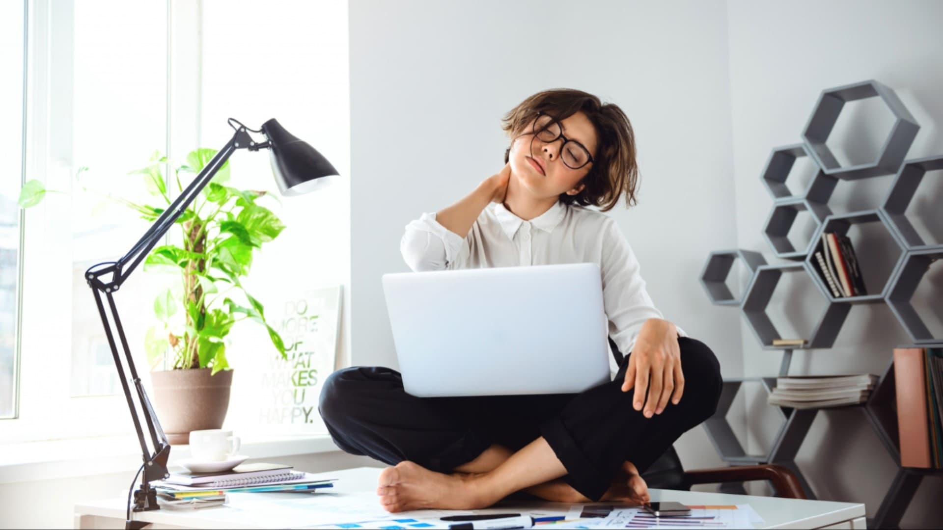 Žena sedí na stole s notebookom a masíruje si krk