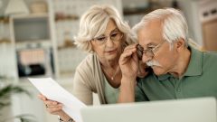 Starší muž a žena v okuliaroch hľadia do papieru.