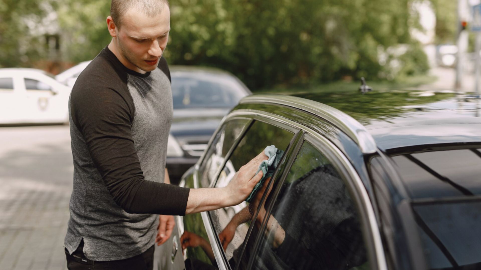 Muž čistí handričkou okno auta.