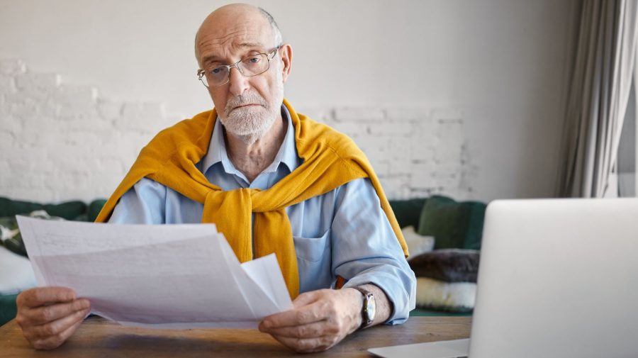 Starší muž s okuliarmi drží v rukách papiere.
