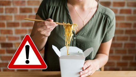 Žena drží paličky a naberá si rezance z krabičky.