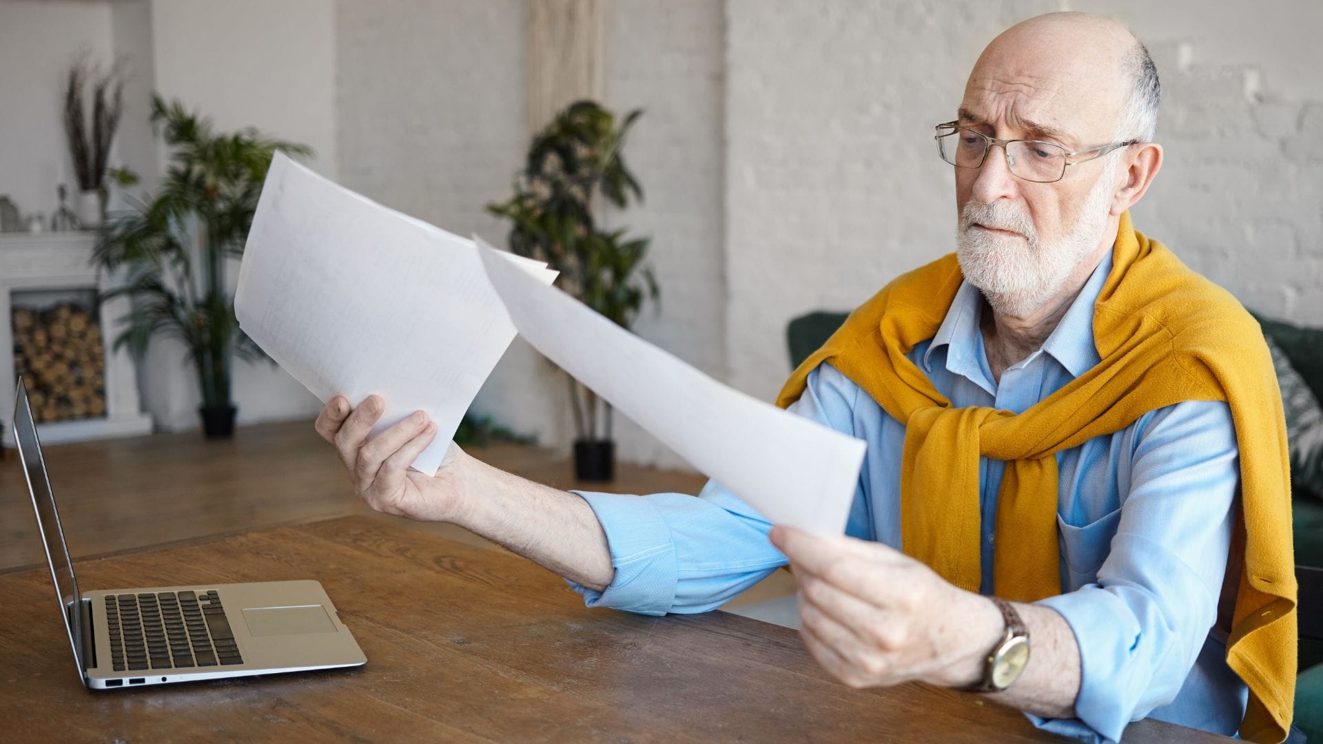 Starší muž za stolom si prezerá papiere.