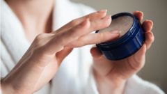 Žena si berie krém z nádobky.