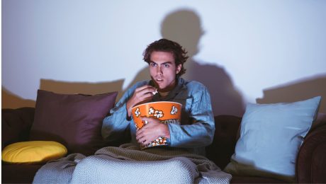 Muž pozerá TV s popcornom v ruke