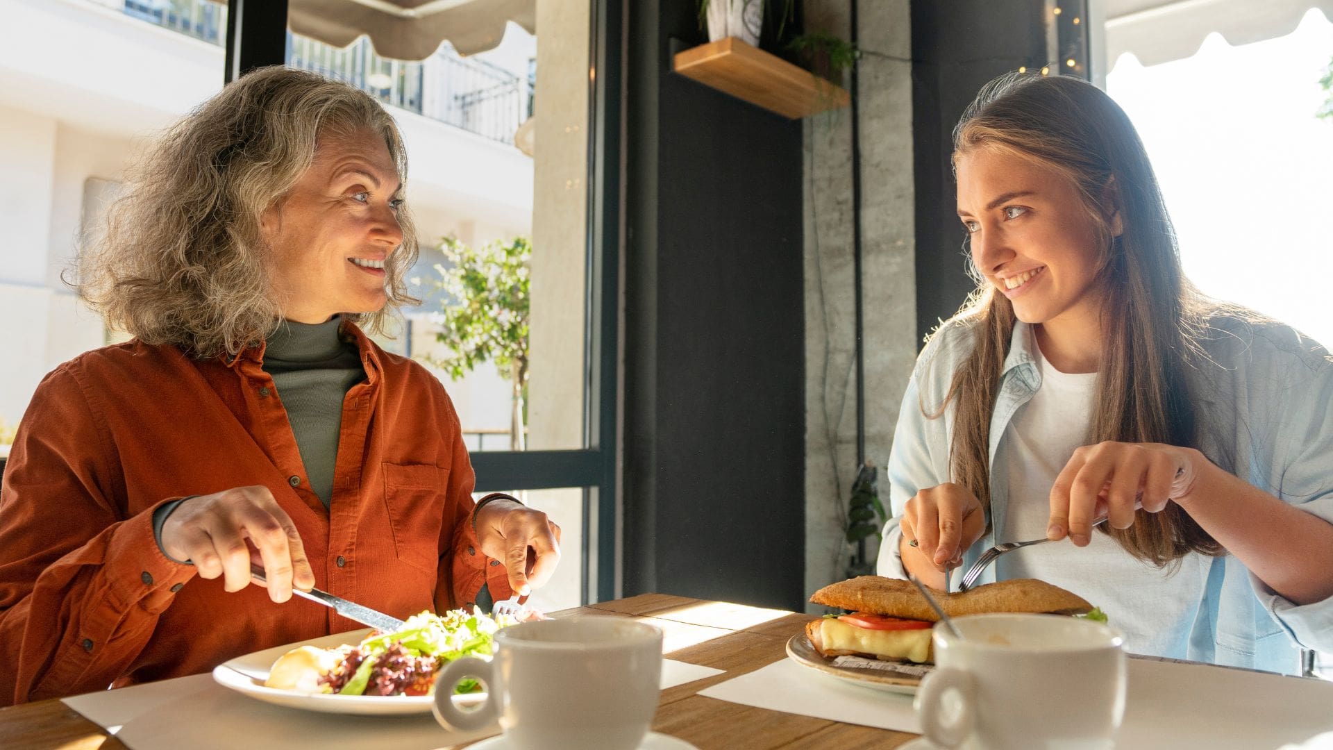 staršia a mladšia žena raňajkujú šalát, vajcia a pečivo