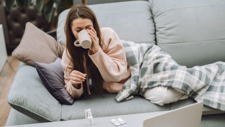 žena leží na gauči a pije čaj, na stole má vitamín C