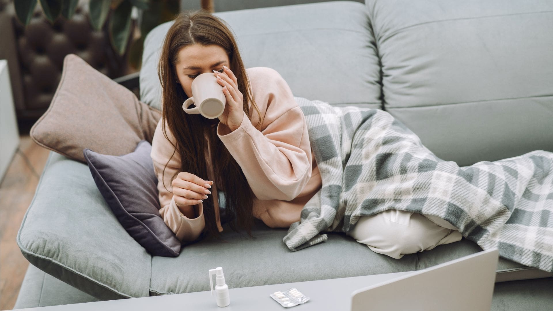 žena leží na gauči a pije čaj, na stole má vitamín C