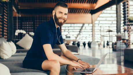 smejúci sa muž počúva hudbu, na stole má notebook
