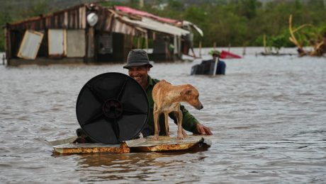Muž sa brodí so svojím psom a s vecami cez zaplavenú ulicu po tom, ako túto oblasť zasiahol hurikán Melissa v Santiagu de Cuba 29. októbra 2025.