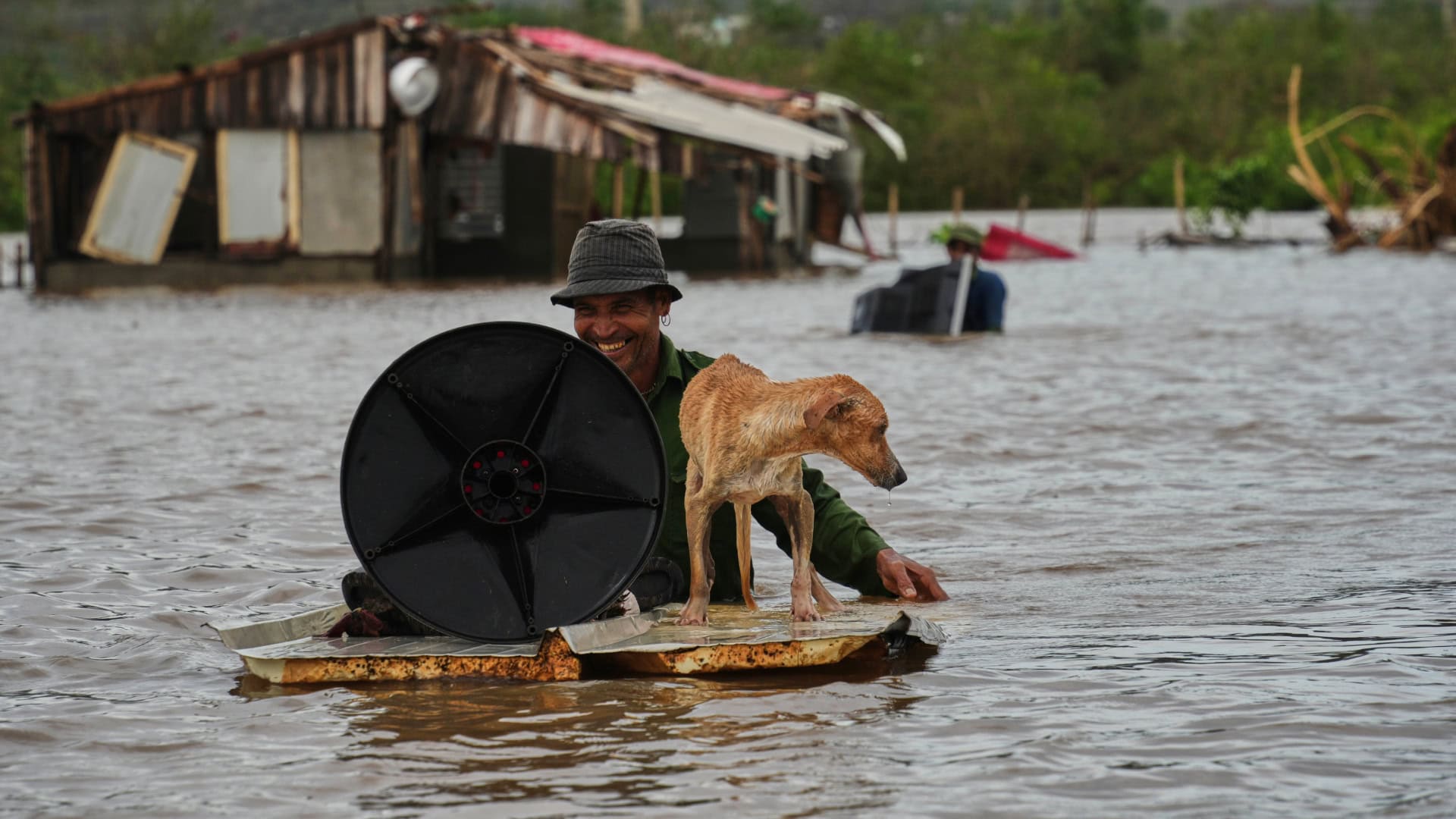 Muž sa brodí so svojím psom a s vecami cez zaplavenú ulicu po tom, ako túto oblasť zasiahol hurikán Melissa v Santiagu de Cuba 29. októbra 2025.