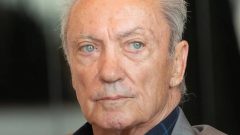 Starší muž s modrými očami, blízky portrét, na pozadí kancelária alebo interiér, profesionálne fotografie, téma biznis a leadership.