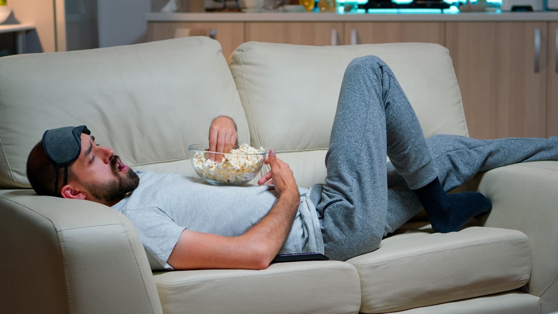 Muž ležiaci na gauči s pukancami v ruke